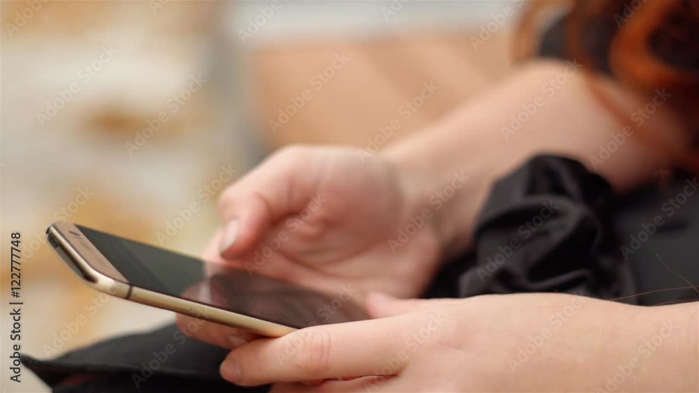 Women's hands are holding touch phone closeup. Girl sitting on a bench reading and talking on the internet. Yellow leaves lie side by side under the bench. Women's hands are holding touch phone closeup. Girl sitting on a bench reading and talking on the internet. Yellow leaves lie side by side under the bench.