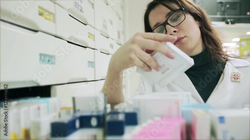 Good looking Pharmacist woman with glasses taking medicine from a drawer