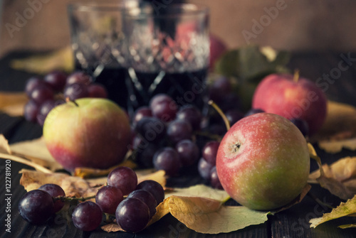 Two glasses with red wine  apples and grapes on a wooden surface