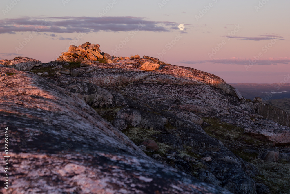 Beautiful soft pink sunset over rock with full moon. Arctic summer, the tundra, Norway.
