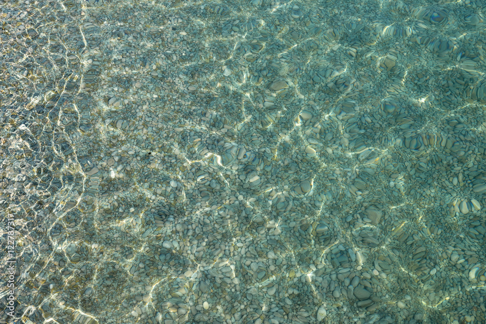 Shimmering sun glares on pebble seabed under water as background Shimmering sun glares on pebble seabed under water as background