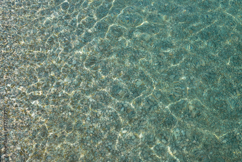 Shimmering sun glares on pebble seabed under water as background