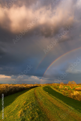 Ominous stormy sky at evening  and beautiful after rain rainbow  in remote rural field