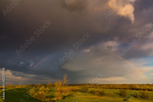 Ominous stormy sky at evening, and beautiful after rain rainbow, in remote rural field © Calin Tatu