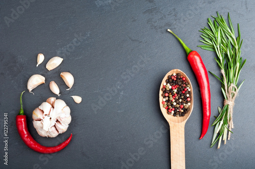 Rosemary, pepper in a spoon, chilli and garlic on a dark stone background. Spices and herbs background with copy space. Top view