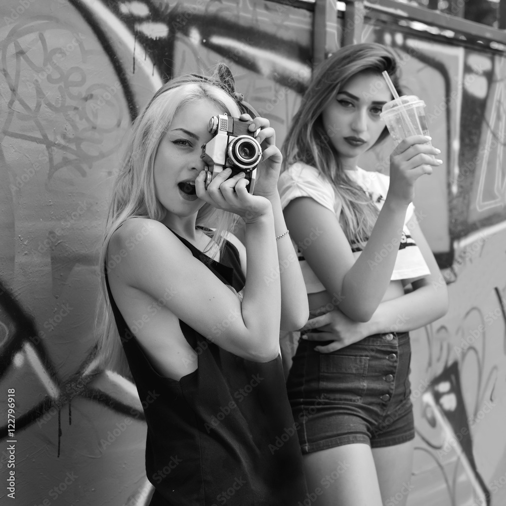 Urban girls have fun with retro vintage photo camera outdoor near grunge wall, black and white image.