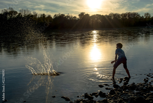 Bub wirft Steine in Fluss bei Sonnenuntergang photo