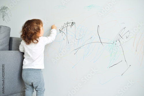 Curly cute little baby girl drawing with crayon color on the wall. Works of child
