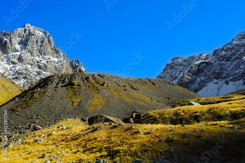 Caucasus Mountains, village Juta. green hill, blue sky, mountain from stones and snowy peak Chaukhebi in summer. 
