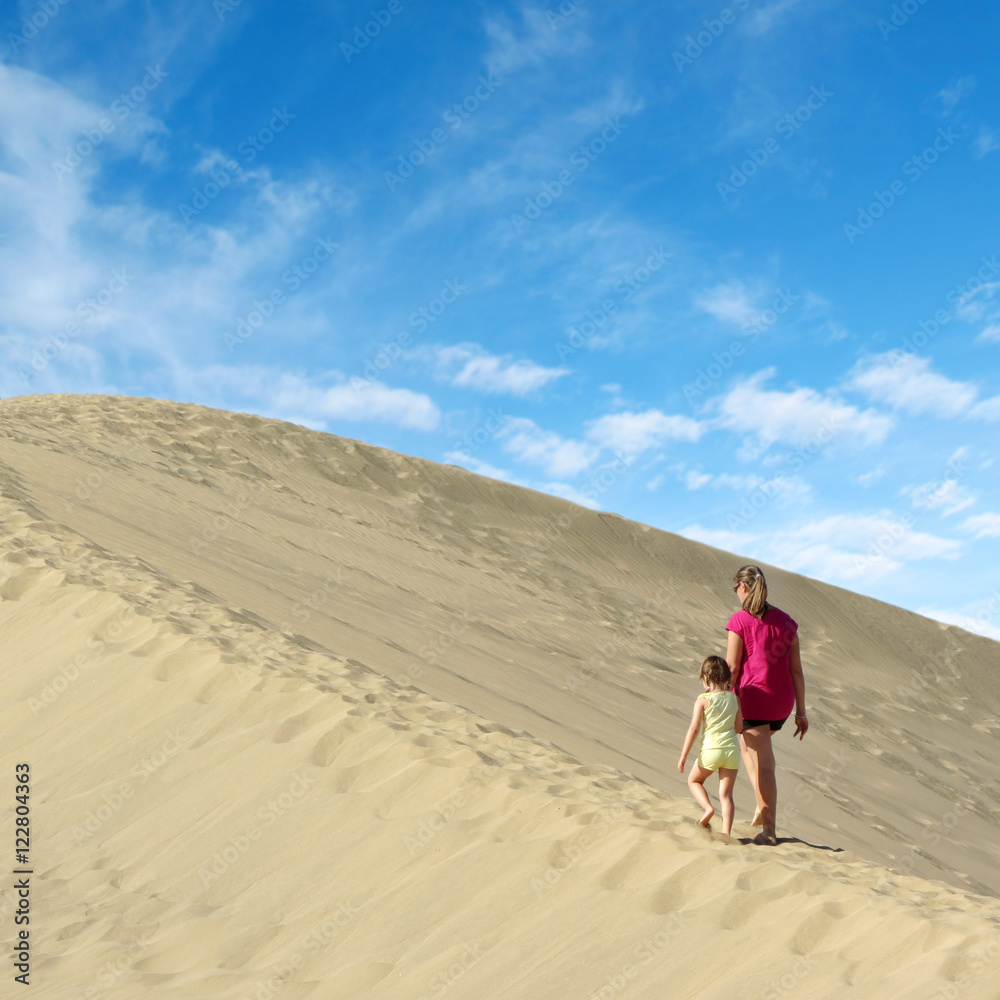 mother and daughter walking on sand dune