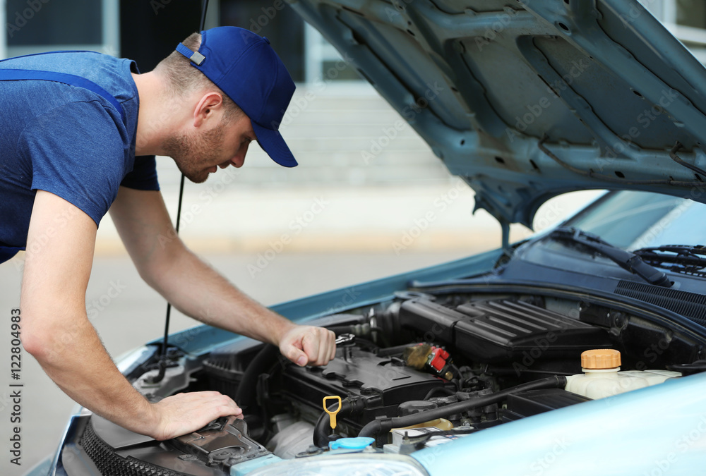 Mechanic standing in front of the open hood and repairing the car Mechanic standing in front of the open hood and repairing the car