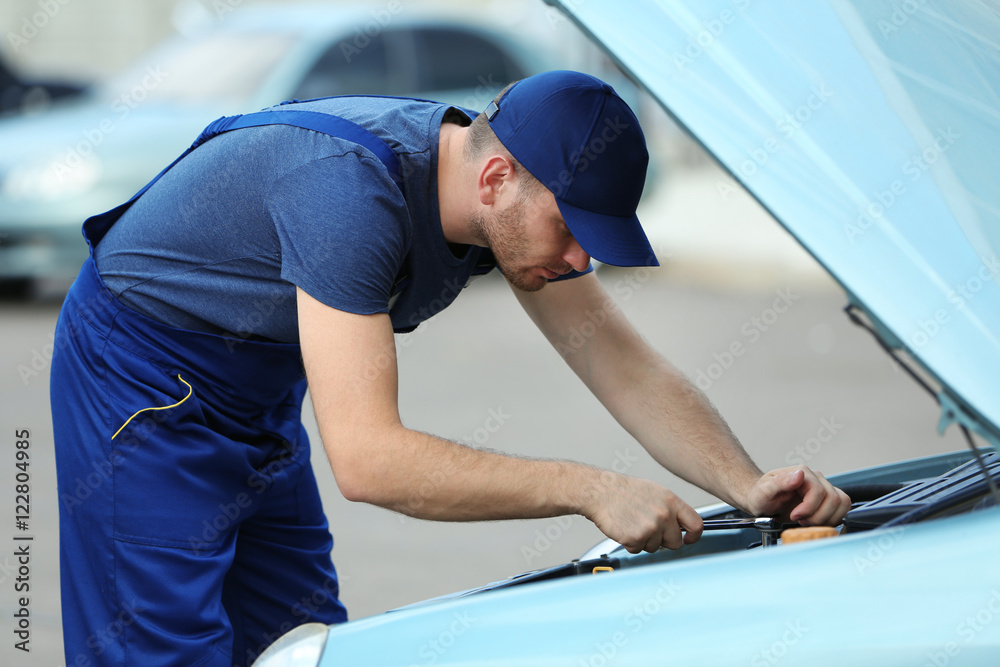 Mechanic standing in front of the open hood and repairing the car Mechanic standing in front of the open hood and repairing the car