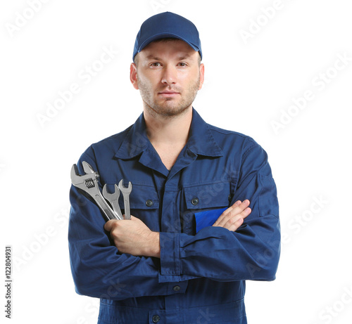 Young mechanic in uniform with crossed arms and wrenches standing, isolated on white