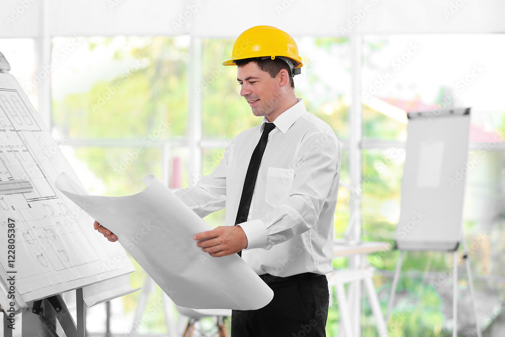 Young creative male engineer with blueprint in design department Young creative male engineer with blueprint in design department