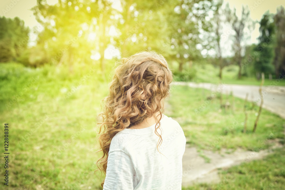Sweet girl outdoors with curly hair in the wind. Back view