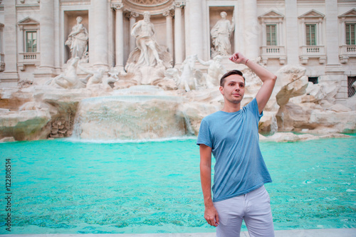Young man tourist trowing coins at Trevi Fountain, Rome, Italy for good luck. Caucasian guy making a wish to come back.