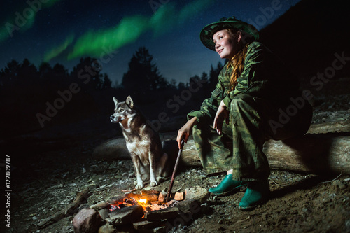 Scout girl with her dog around campfire at night stars and aurora borealis