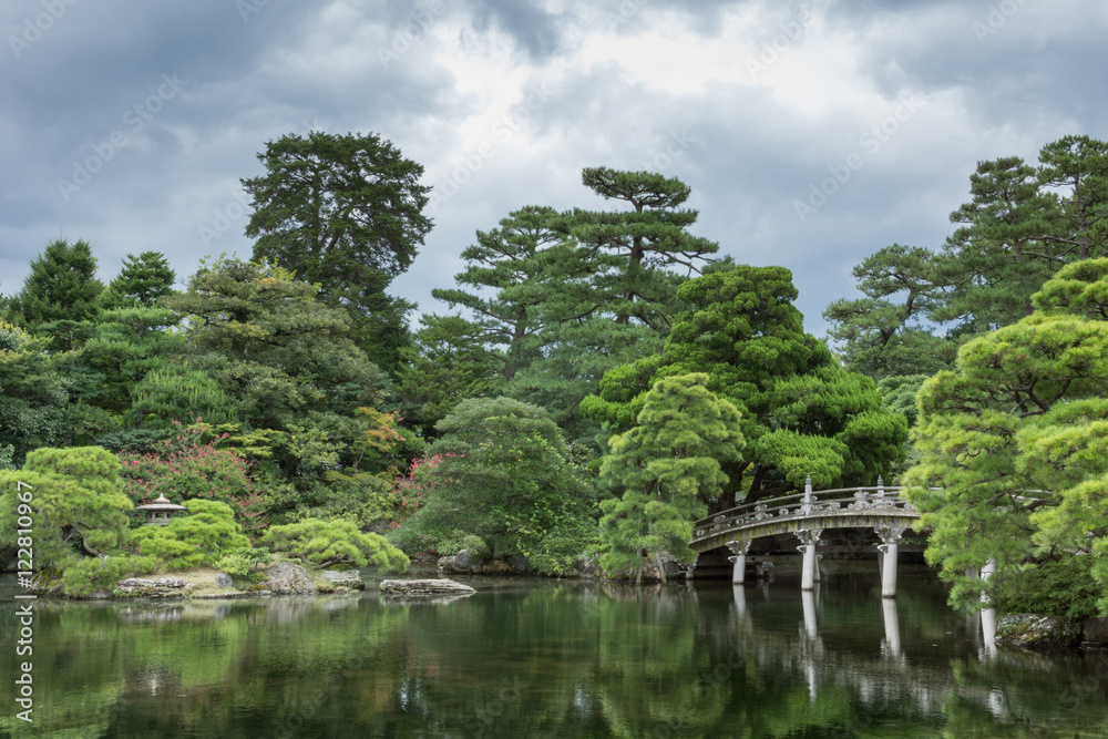 Kyoto, Japan - September 14, 2016: Part of the Japanese garden at the imperial palace showing bridge, pond, trees and flowers under heavy sky.