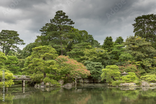 Kyoto, Japan - September 14, 2016: Part of the Japanese garden at the imperial palace showing bridge, pond, trees and flowers under heavy sky.