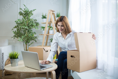 Billede på lærred home, post, delivery and happiness concept - smiling young woman opening cardboa