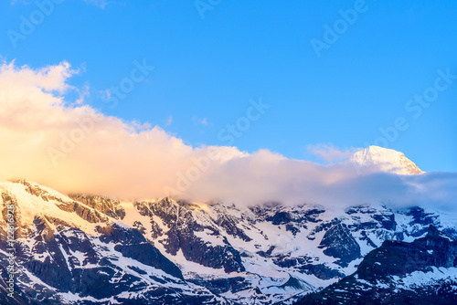 View of beautiful Alps with snow-capped mountain tops and nice clouds at sunset. © karamysh