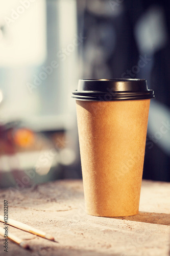 Disposable coffee cup with art brushes on table in artists studio space, soft sunshine and worm colors.