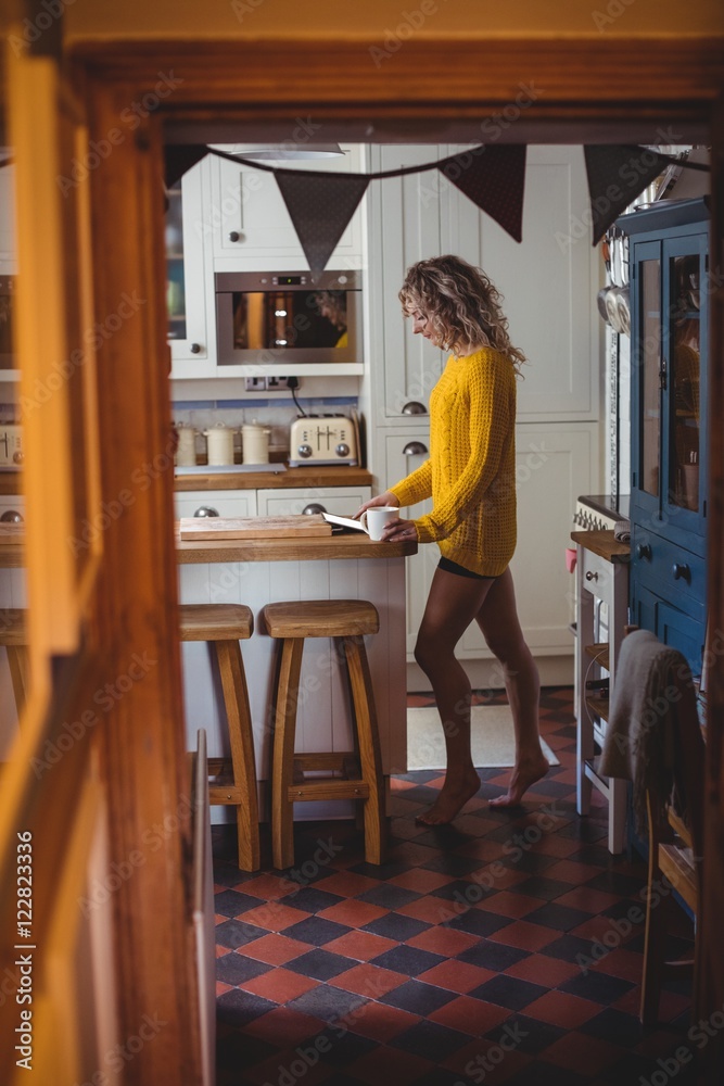 Beautiful woman using digital tablet while having coffee in kitc Beautiful woman using digital tablet while having coffee in kitc
