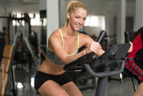 Young Women On Bicycle In Fitness Gym