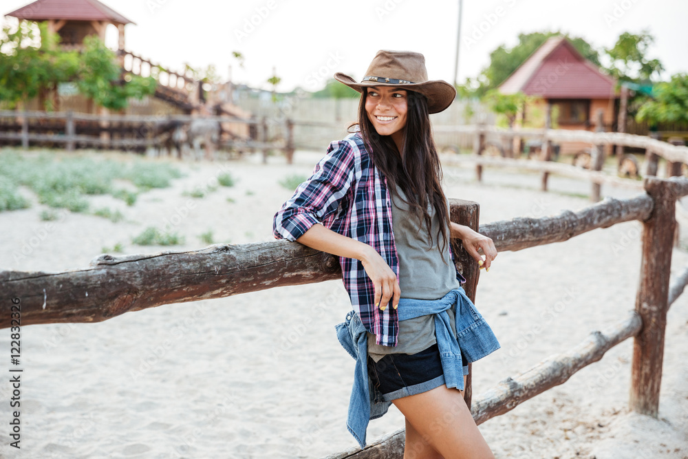 Smiling woman cowgirl standing and leaning on fence