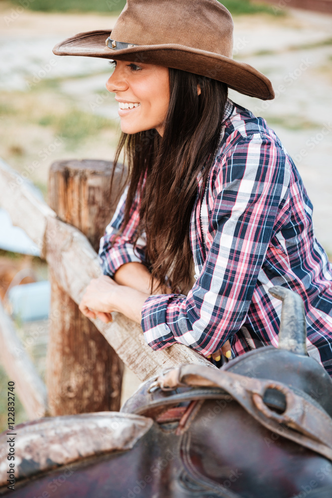 Close up portrait of a smiling cowgirl leaning on fence