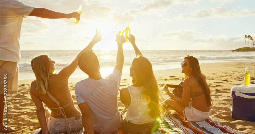 Group of friends having fun enjoying a beverage and relaxing on the beach at sunset