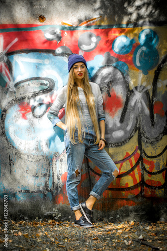 Fashionable girl with long blond hair in stylish clothes standing on a background of graffiti