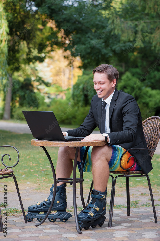 Work and relax. Businessman dressed in suit, shorts and rollers working with laptop at the outdoors cafe Work and relax. Businessman dressed in suit, shorts and rollers working with laptop at the outdoors cafe