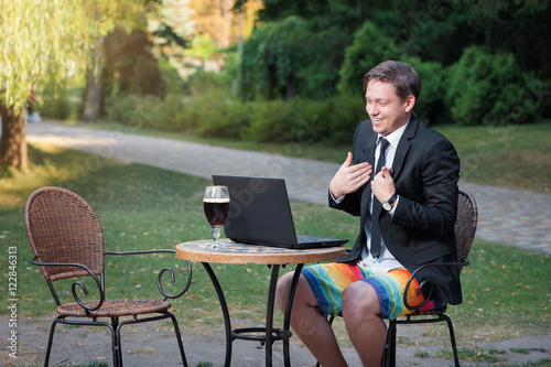 Work and relax. Online conference. Businessman dressed in suit and shorts working with laptop, talking by skype at the park cafe outdoors photo