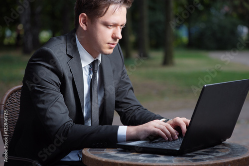Focused businessman. Attractive young man in formal wear working on laptop while sitting at the table outdoors.