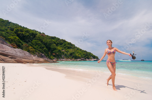 Happy tropical vacation on white sand. Beach woman walking by ocean. Girl in bikini with snorkel coming out of water after swimming and snorkeling in beautiful blue sea on Similan Island, Thailand.