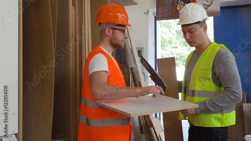 Two carpenters are analyzing construction plans while looking at the wooden desks.
