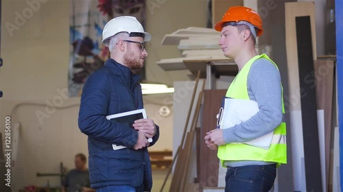 A supervisor is giving a handshake to carpenter in carpentry shop. They're holding a documents and tablet pc.