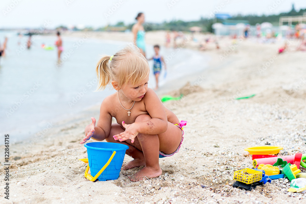 Adorable toddler girl playing with beach toys on white sand beach