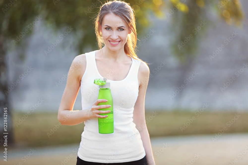 Fototapeta premium Young sporty woman drinking water in a park