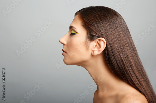 Portrait of young beautiful woman with colourful eye makeup on grey background