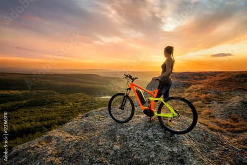 Sunset from the top / A woman with a bike enjoys the view of sunset over an autumn forest