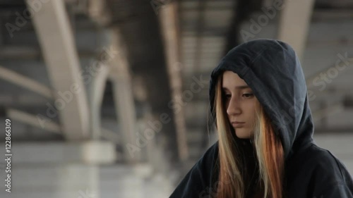 Skater style teenage girl in a hoody with the hood on and loose multicolored hair against the unfocused bridge pillar perspective receding into the distance.