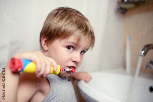 Little boy brushing teeth in bath with electric brush