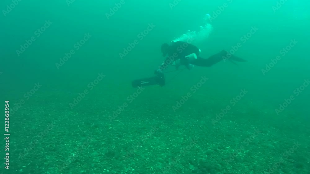 The diver is moving on an underwater scooter over the the seabed, wide shot.
