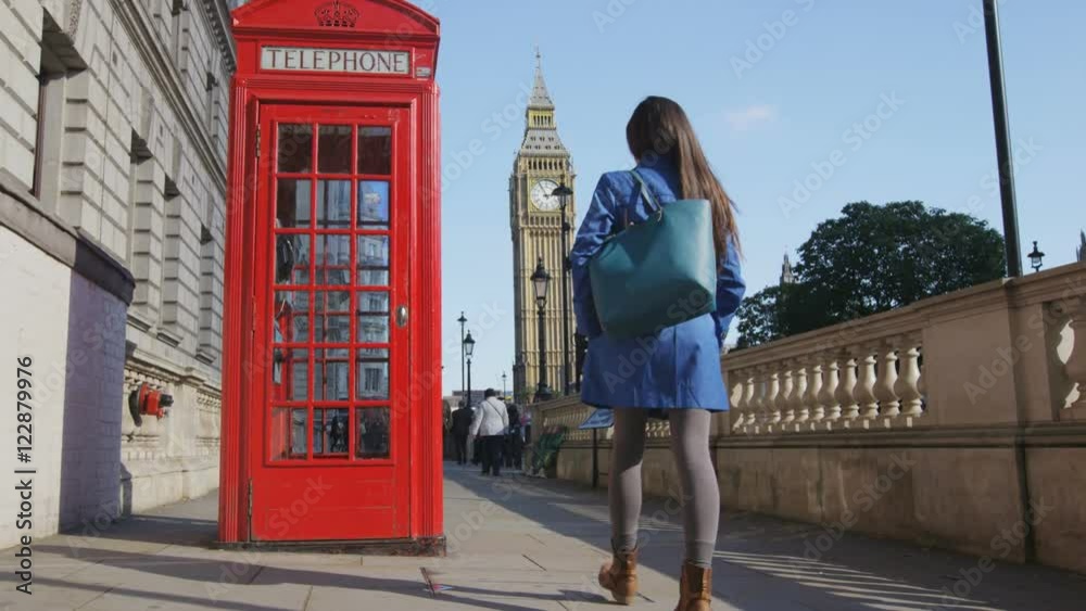 Young female urban professional by red telephone booth and Big Ben in London, England, Great Britain. Casual business woman in trench coat walking in street enjoying leisure time in United Kingdom.