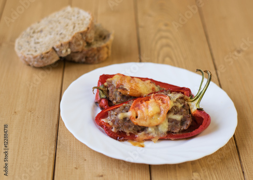 Baked pepper with meat, cheese and tomato on the plate on a wooden table.