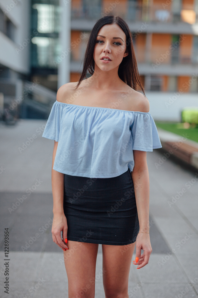 Woman is standing and looking at the camera. Urban background