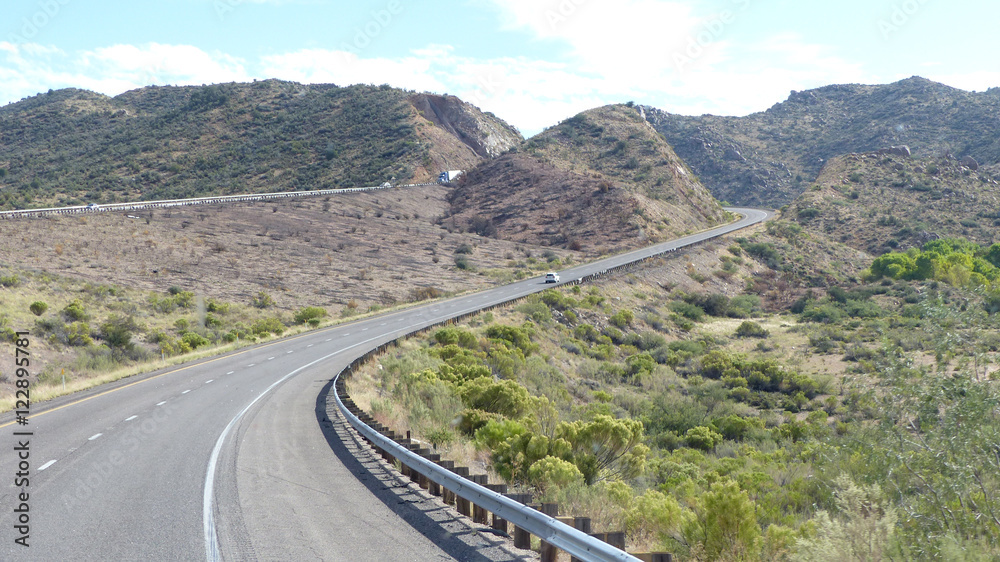 Bergige Wüstenlandschaft / Kurvenreiche Autobahn durch bergige Wüstenlandschaft in Arizona, Vereinigte Staaten von Amerika, zweispurige Fahrbahn mit Markierung