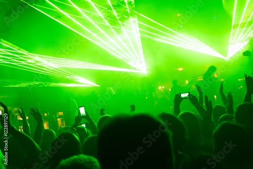 Rock concert, silhouettes of happy people raising up hands in front of bright, green stage laser lights. Space in top side.
